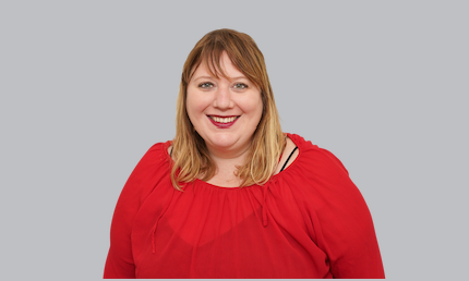 Smiling lady with blonde hair wearing a red shirt on a grey background.